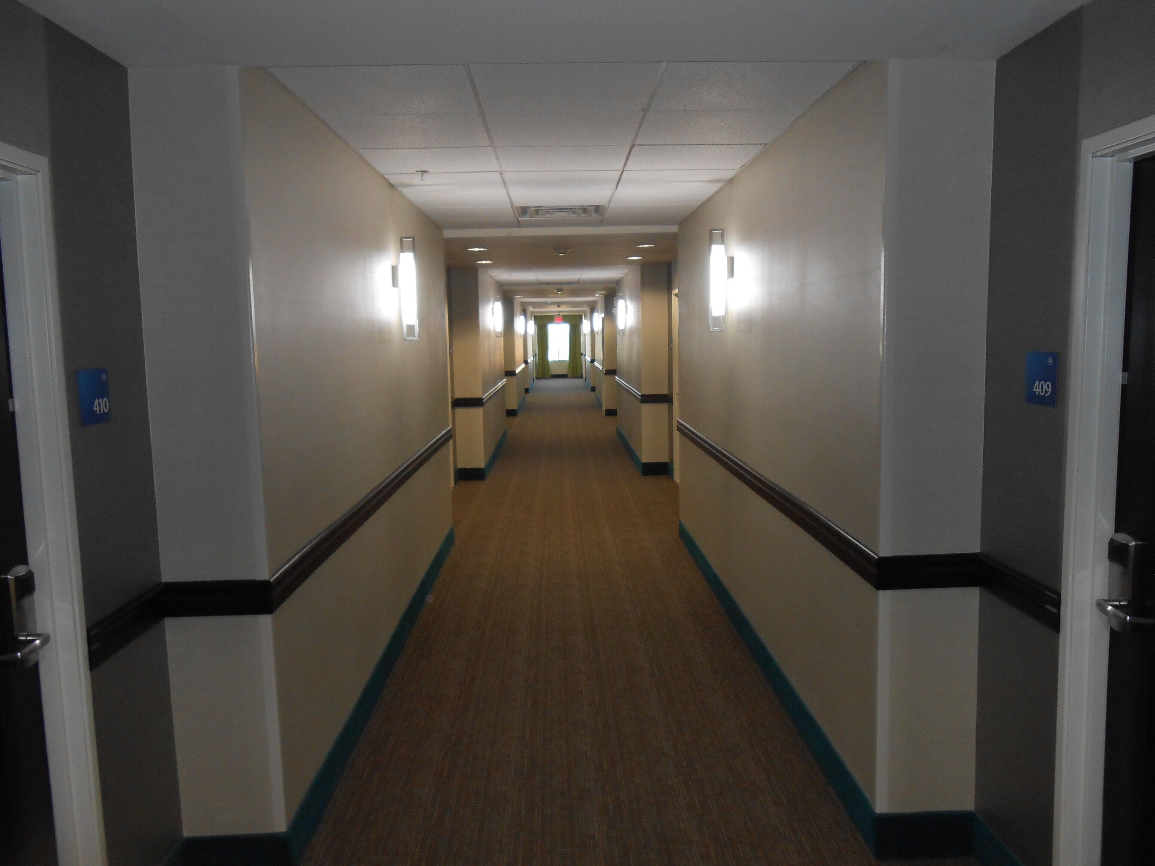 A hotel corridor with a carpeted floor, light-colored walls, and doors marked with room numbers.