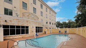 A swimming pool with a stone wall and a building with multiple windows in the background.