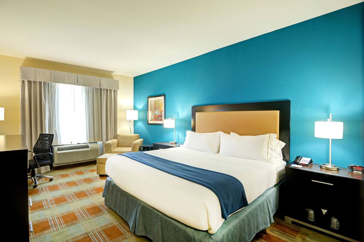 A hotel room with a large bed, a desk with a lamp, a chair, and a nightstand with a phone.