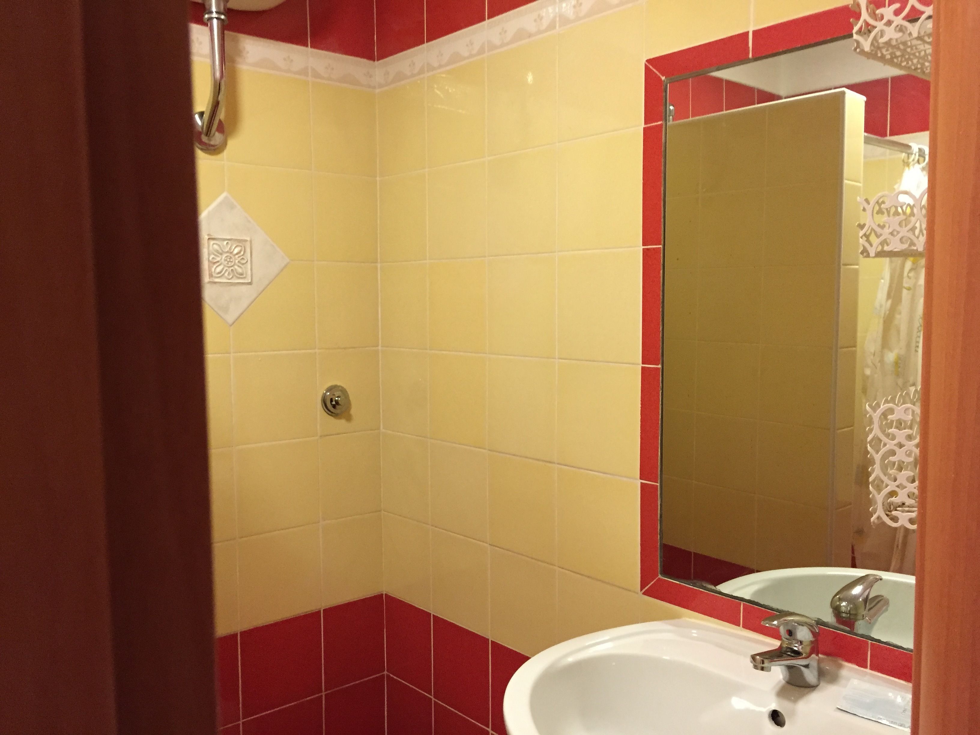 A bathroom with yellow and red tiles, a white sink, and a mirror with a red frame.