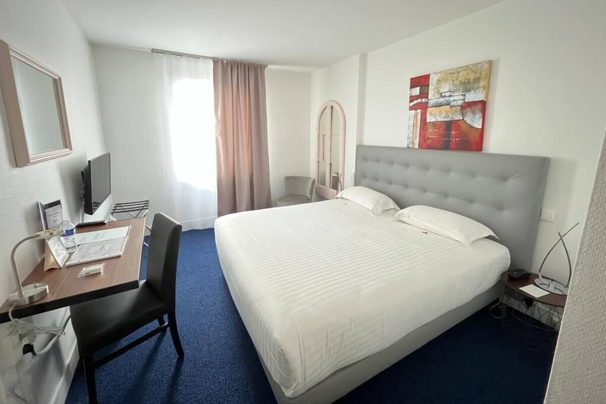 A hotel room with a large bed, a desk with a chair, a television, and a window with curtains.