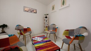 A cozy living room with a colorful striped coffee table, two patterned armchairs, a small bookshelf, and a potted plant. - Hotel le Beffroi (Dreux)