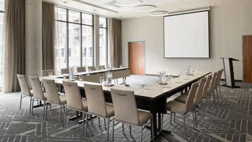 A conference room with a long table, chairs, a projector screen, and a large window with curtains.