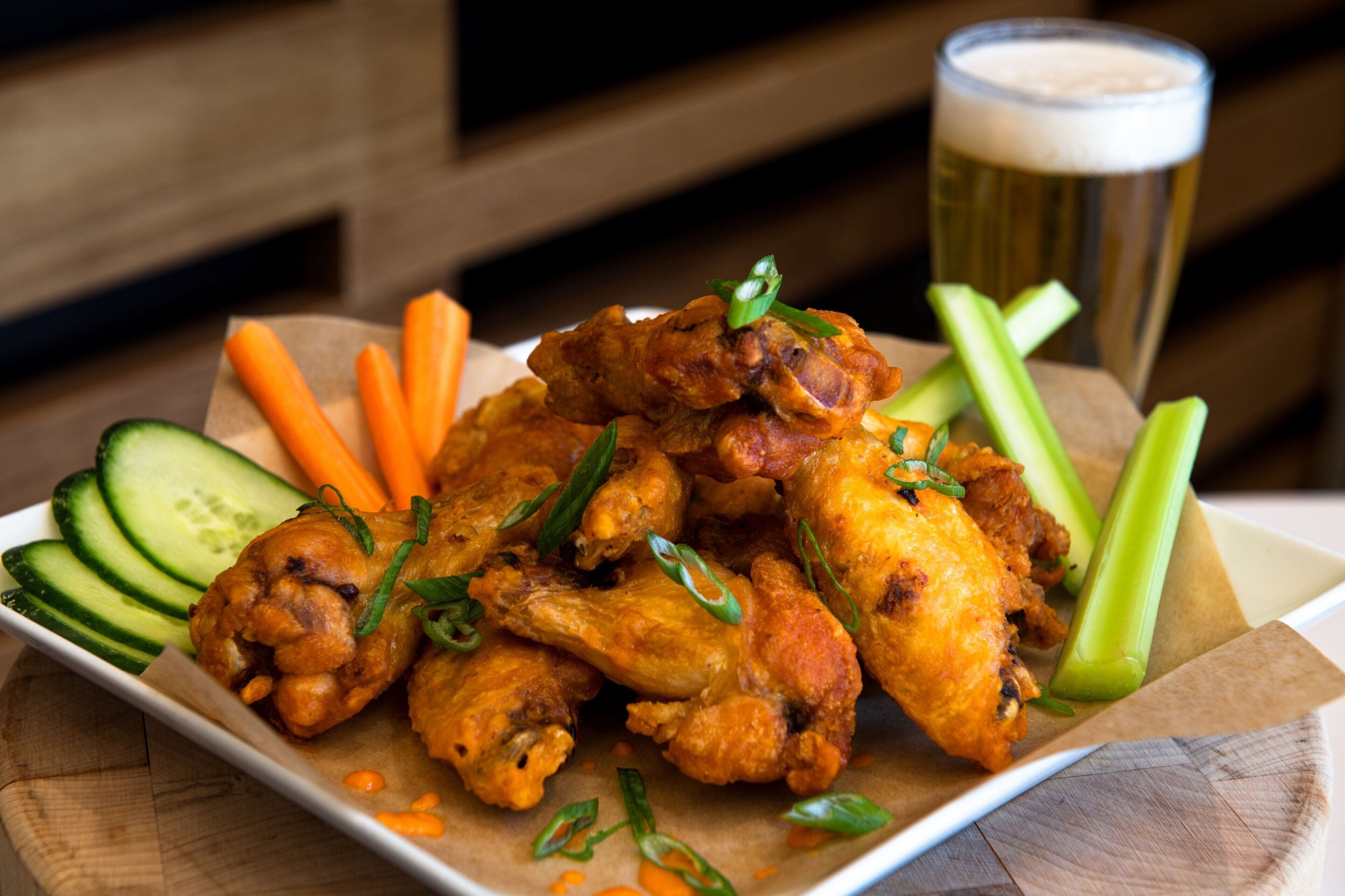 A plate of chicken wings with celery and carrots, accompanied by a glass of beer.