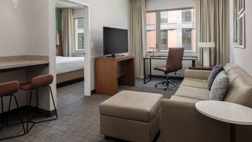 A hotel room with a bed, a desk with a TV, a sofa, a small table, and a chair.