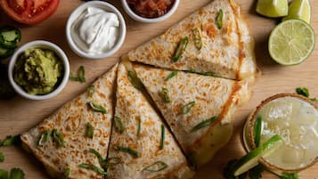 A quesadilla with toppings and sides on a wooden board.