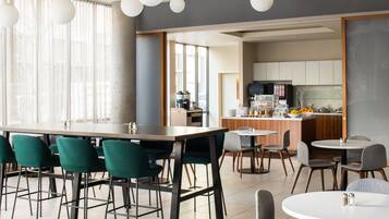 A modern dining area with a bar, green and grey chairs, and a kitchen in the background.