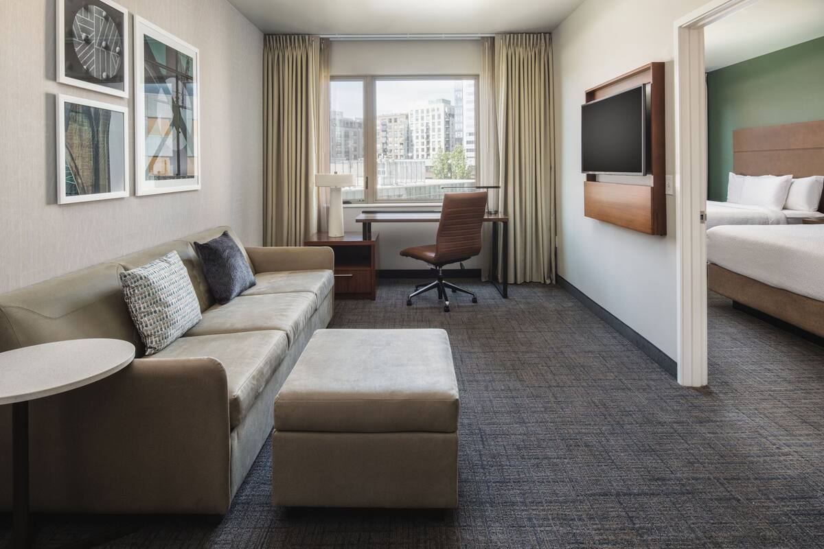 Habitación de hotel con sofá, reposapiés, escritorio, silla, televisión y cama.