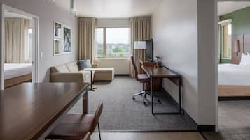 A hotel room with a bed, a desk with a chair, a sofa, a TV, and a window with curtains.