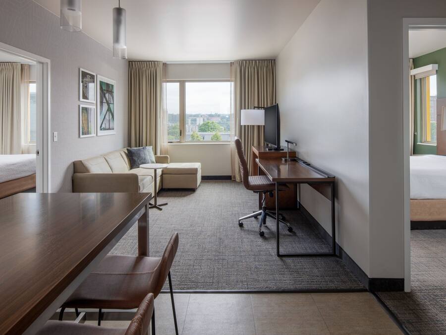 A hotel room with a bed, a desk with a chair, a sofa, a TV, and a window with curtains.