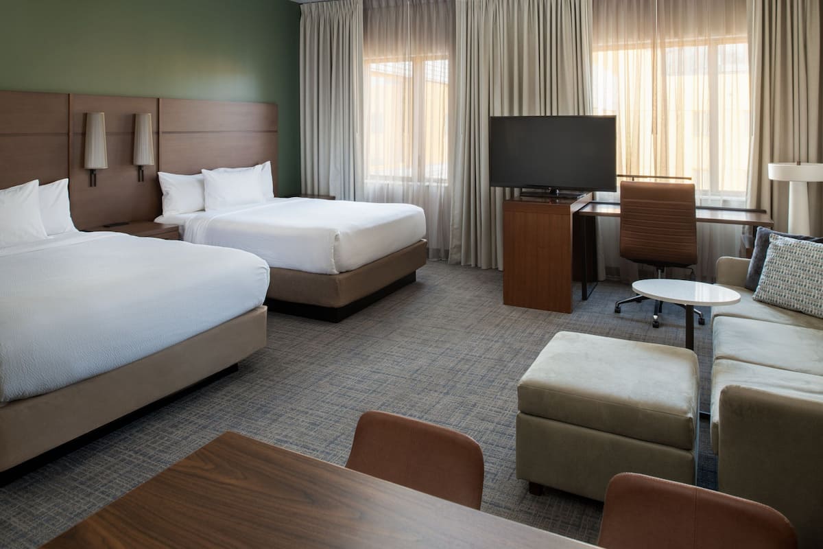 Habitación de hotel con dos camas, televisión, escritorio y zona de estar.