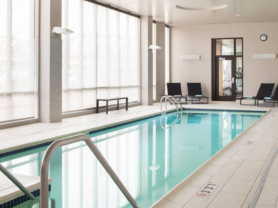 An indoor swimming pool with clear glass walls, a tiled floor, and a few lounge chairs.