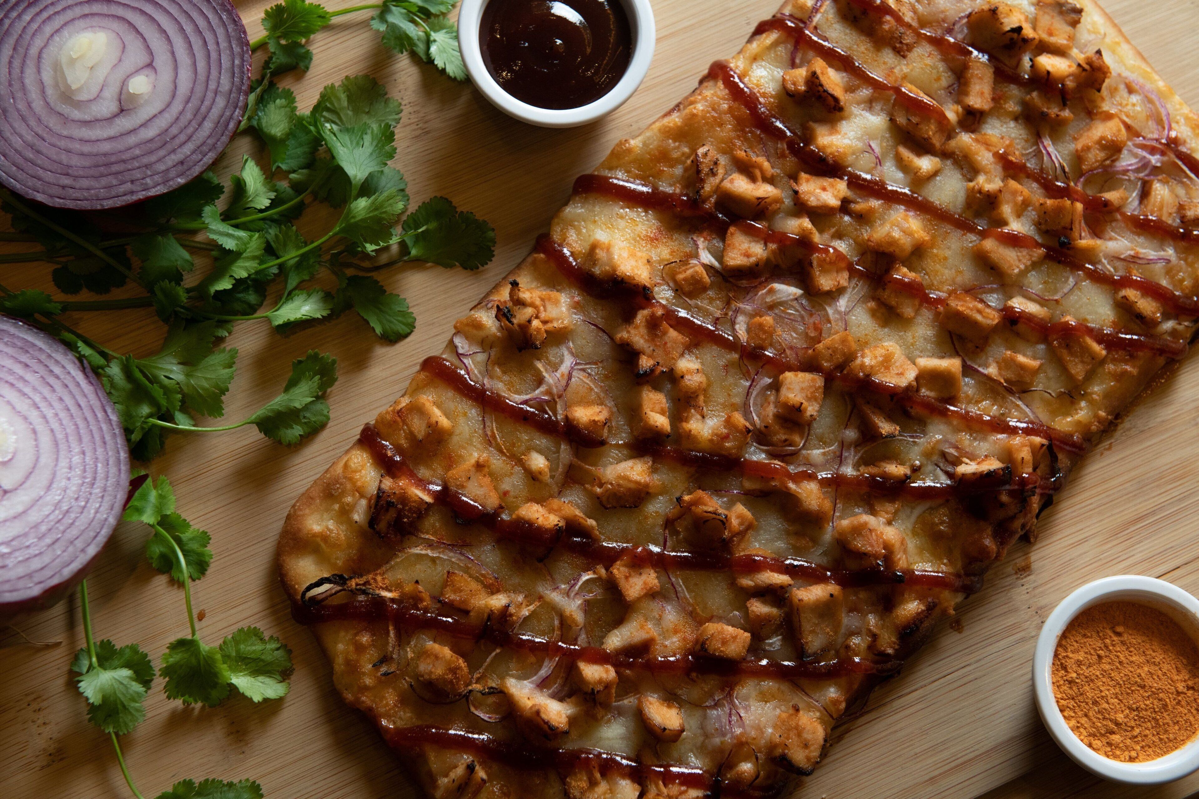 A flatbread with toppings and sauces on a wooden surface.