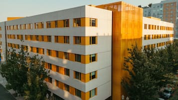 Un bâtiment moderne à plusieurs étages, doté d’une façade blanche et de touches de couleur orange, entouré d’arbres et d’autres bâtiments.