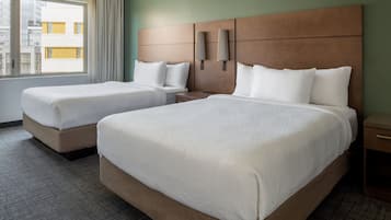 Una habitación de hotel con dos camas, un ventanal con cortinas, cabecero con apliques de pared y suelo alfombrado.