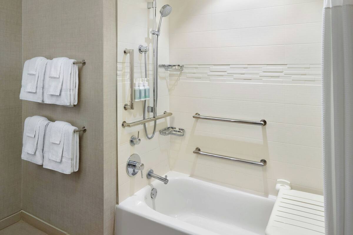 Un baño moderno con bañera, dos toalleros, un cabezal de ducha y un pasamanos.