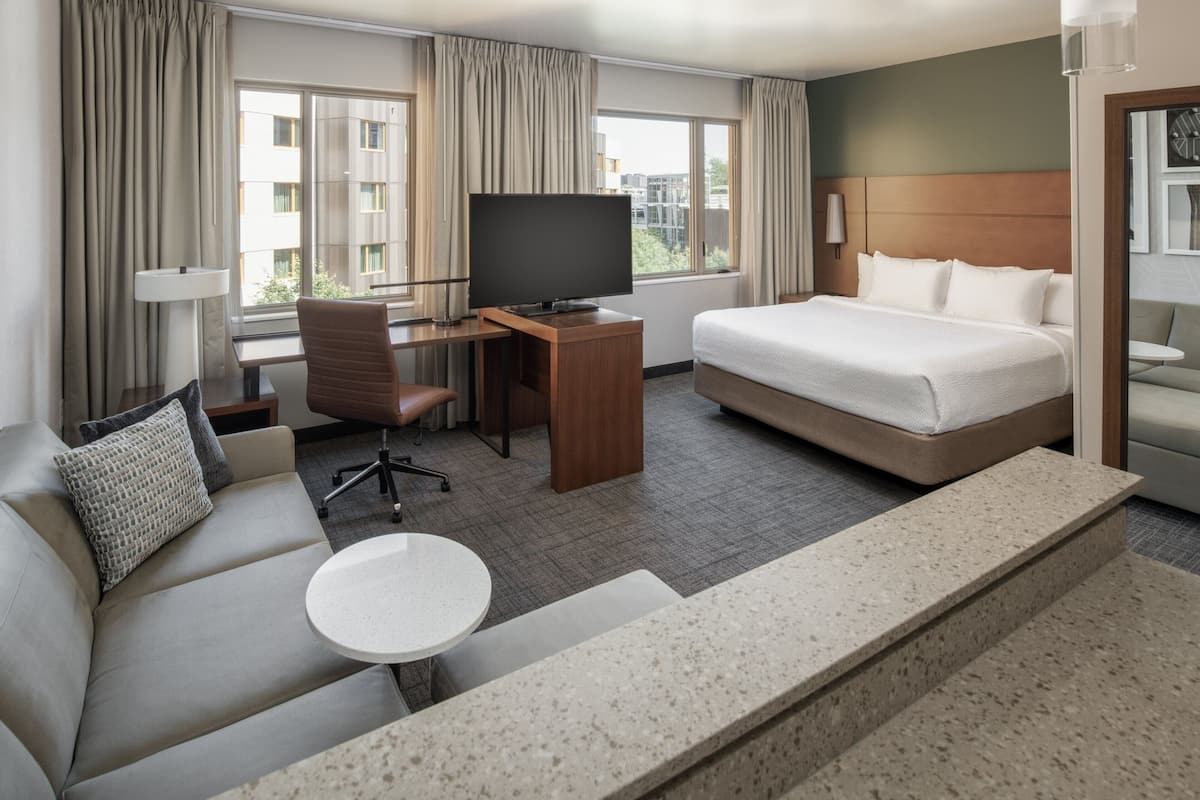 Una habitación de hotel con cama, escritorio con televisor, sofá y una mesita.