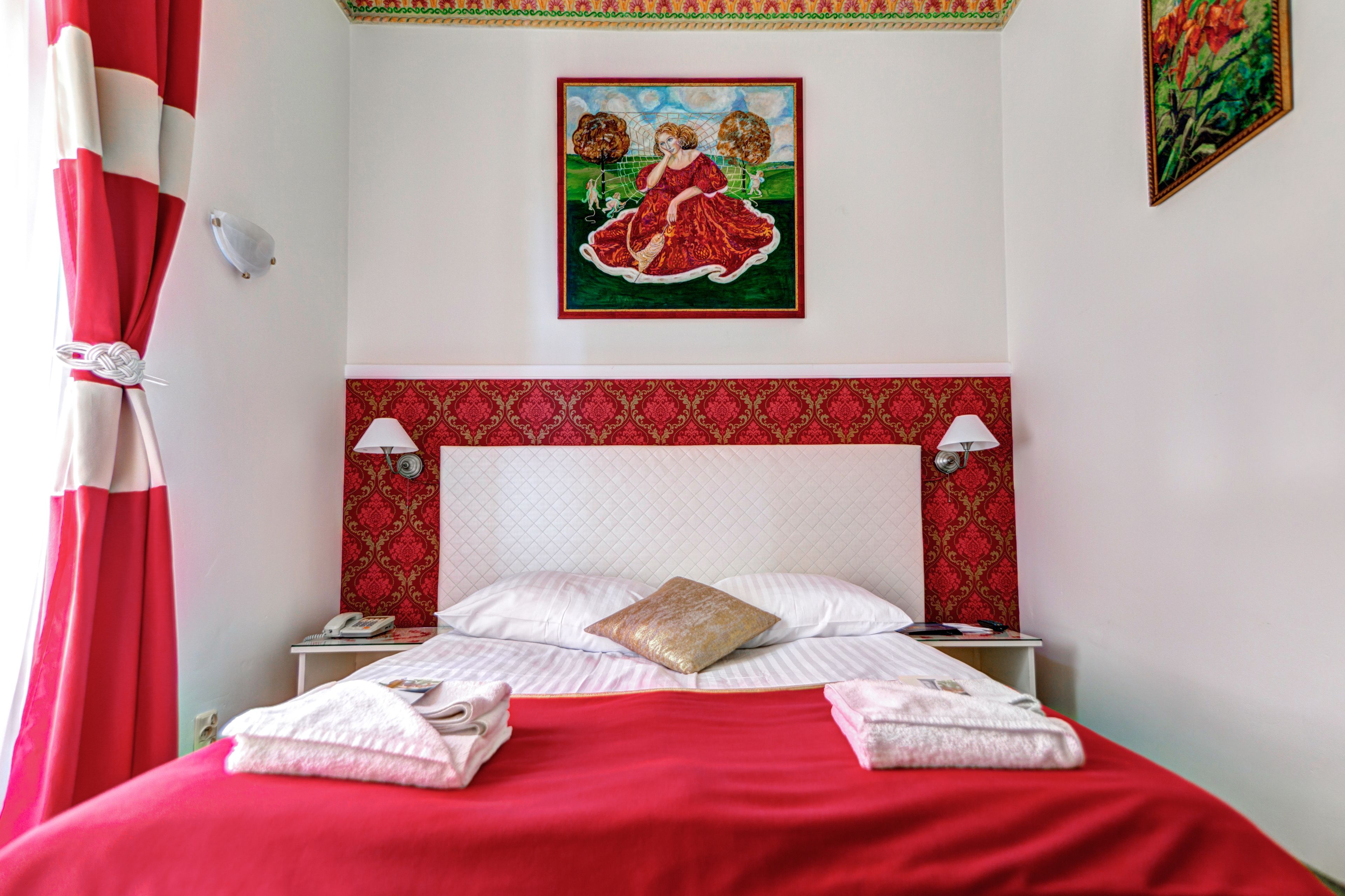Habitación de hotel con una colcha roja, un cabecero estampado, dos lámparas de noche y un cuadro en la pared.