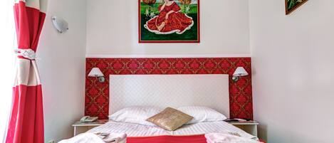 A hotel room with a red bedspread, a patterned headboard, two bedside lamps, and a painting on the wall.