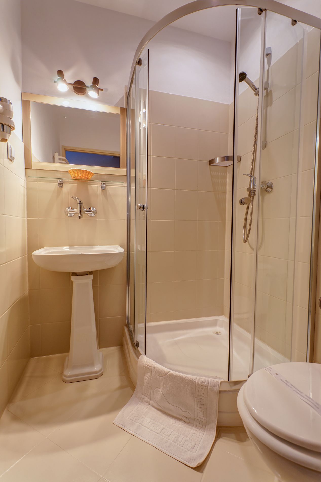 A modern bathroom with a glass-enclosed shower, a pedestal sink, and a toilet.