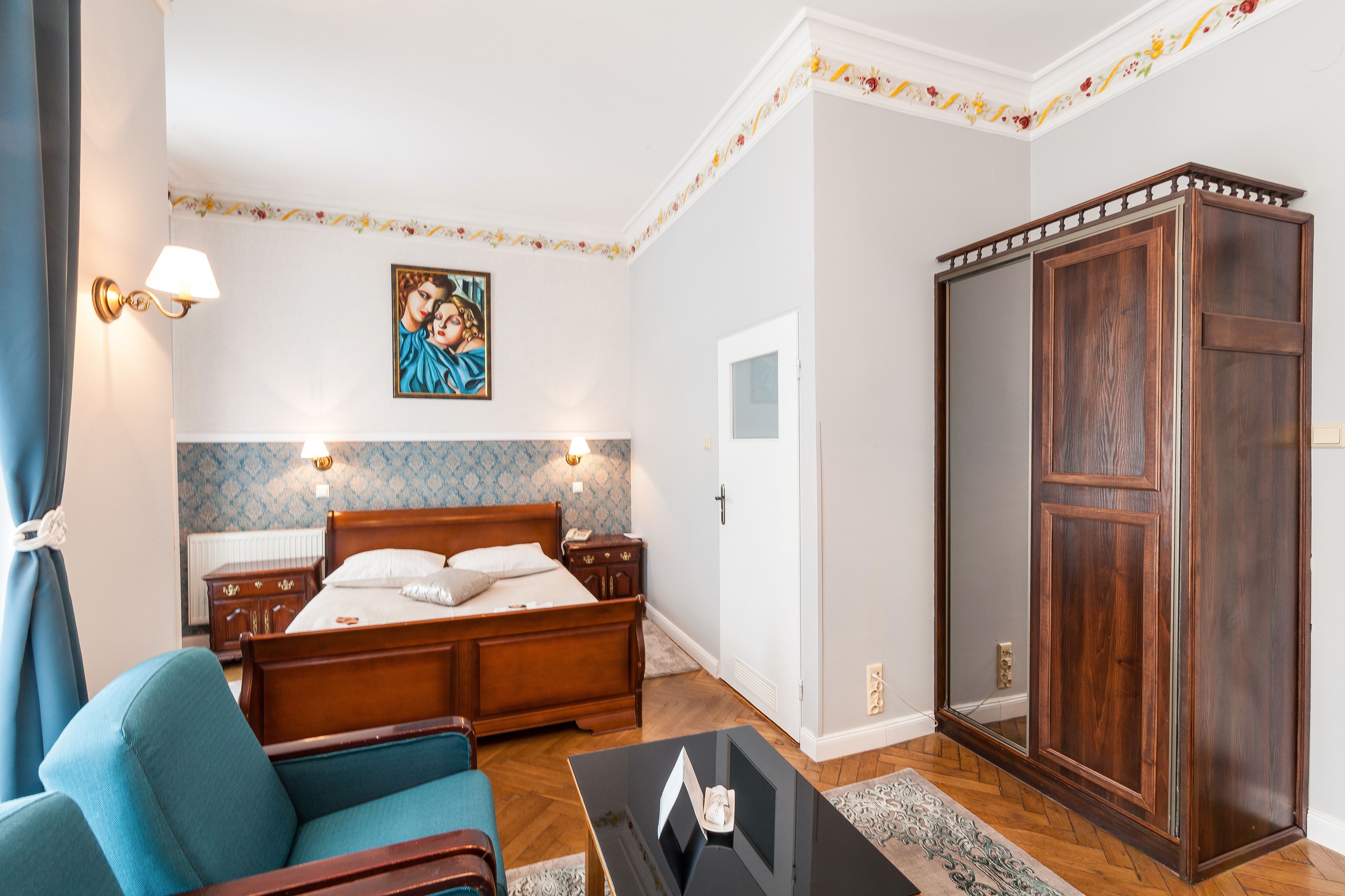 A bedroom with a wooden bed, a blue armchair, a wardrobe, and a painting on the wall.