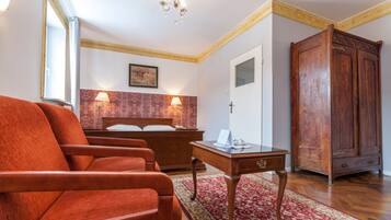 A hotel room with a large wooden wardrobe, a bed with a red headboard, two bedside lamps, and a red armchair.