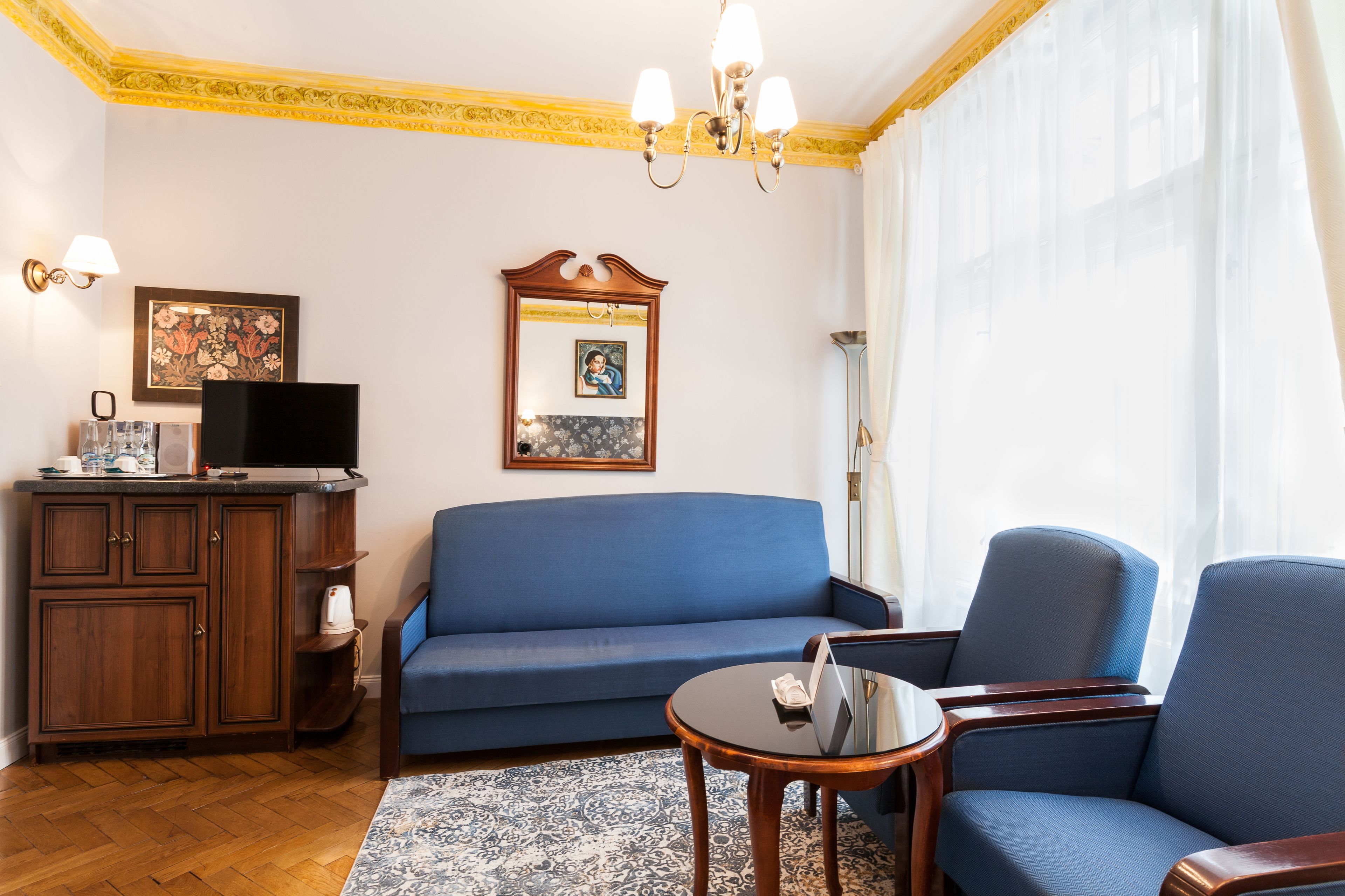 A living room with a blue sofa, a wooden cabinet, a flat-screen TV, and a chandelier.