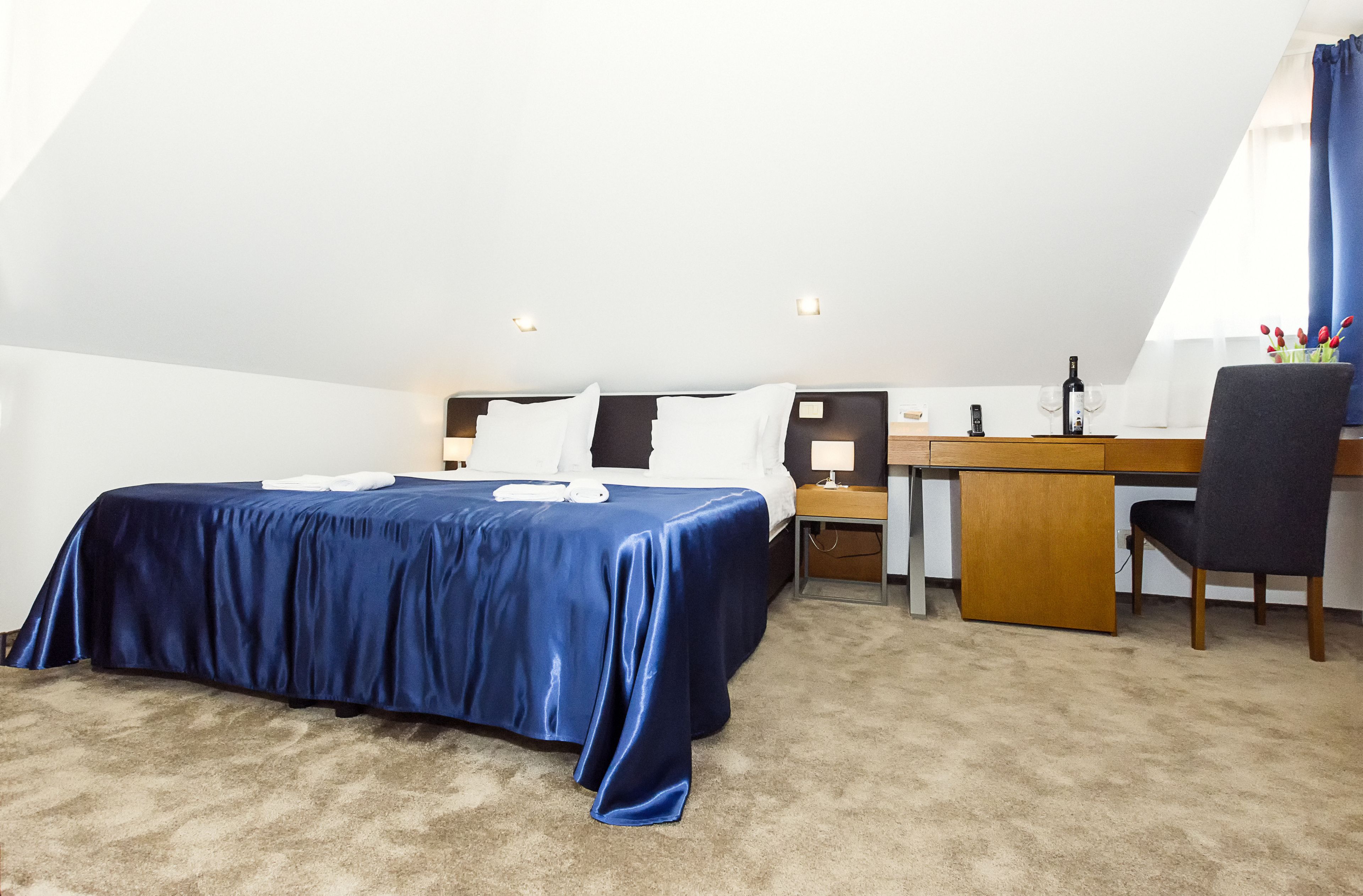 A bedroom with a bed, desk, chair, and a window with curtains.