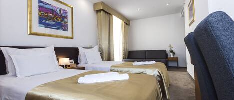 A hotel room with two beds, a large window with curtains, a desk with a lamp, and a chair.