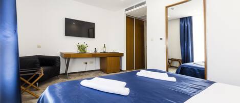 A hotel room with a large bed, a desk with a mirror, a TV, and a wardrobe.