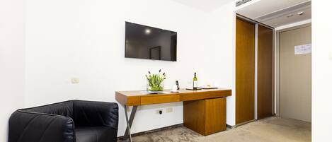 A modern hotel room with a black leather sofa, a wooden desk with a mirror, and a small plant.