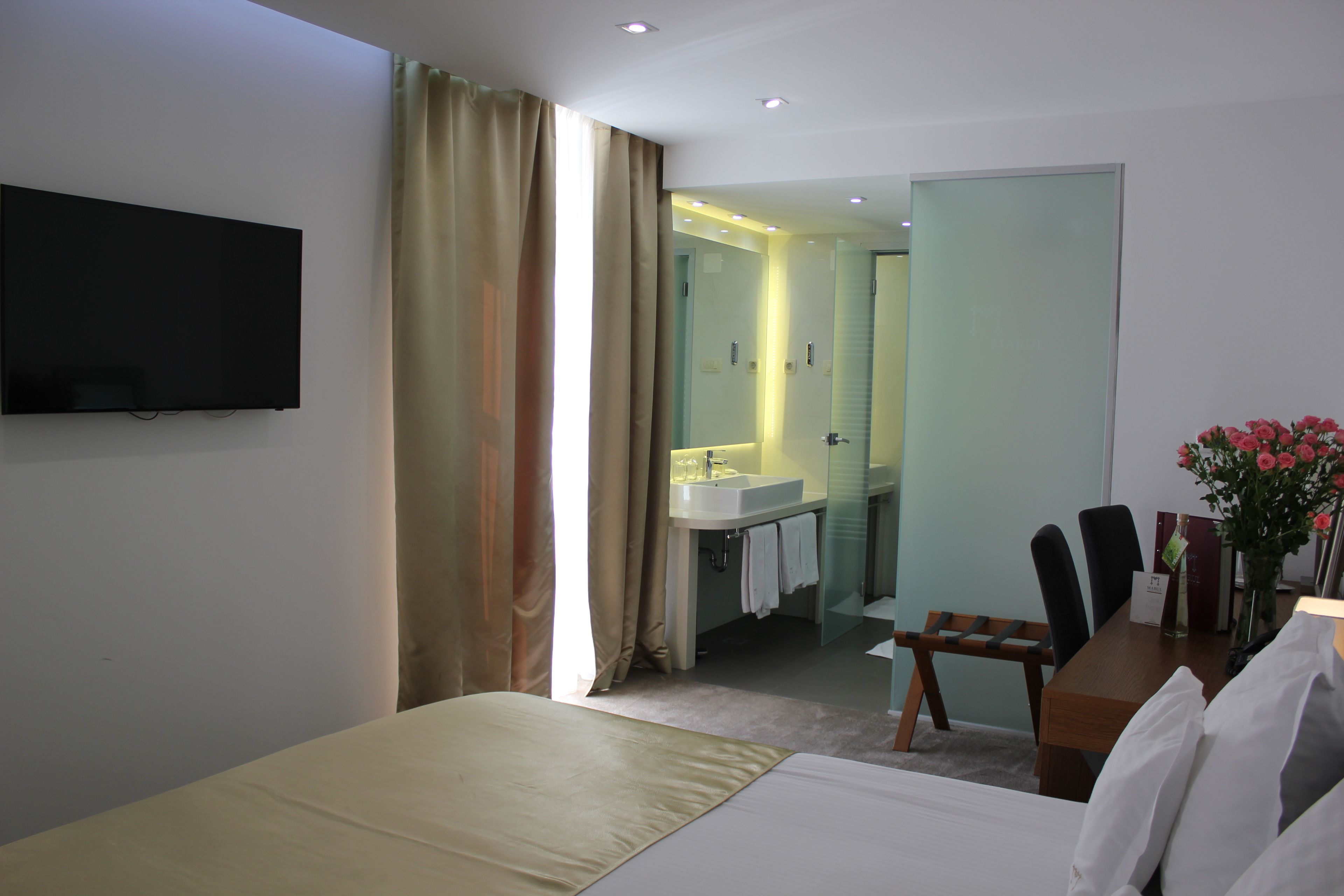 Habitació d'hotel amb llit, televisió penjada a la paret, bany amb rentapla i mirall, i zona de menjador amb taula i cadires.