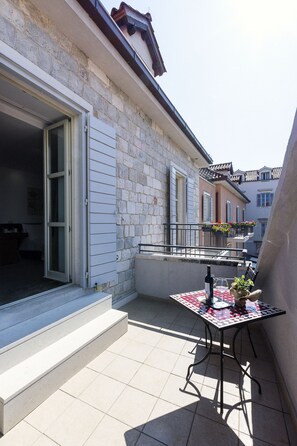 A balcony with a tiled floor, a table with a checkered tablecloth, and a potted plant.