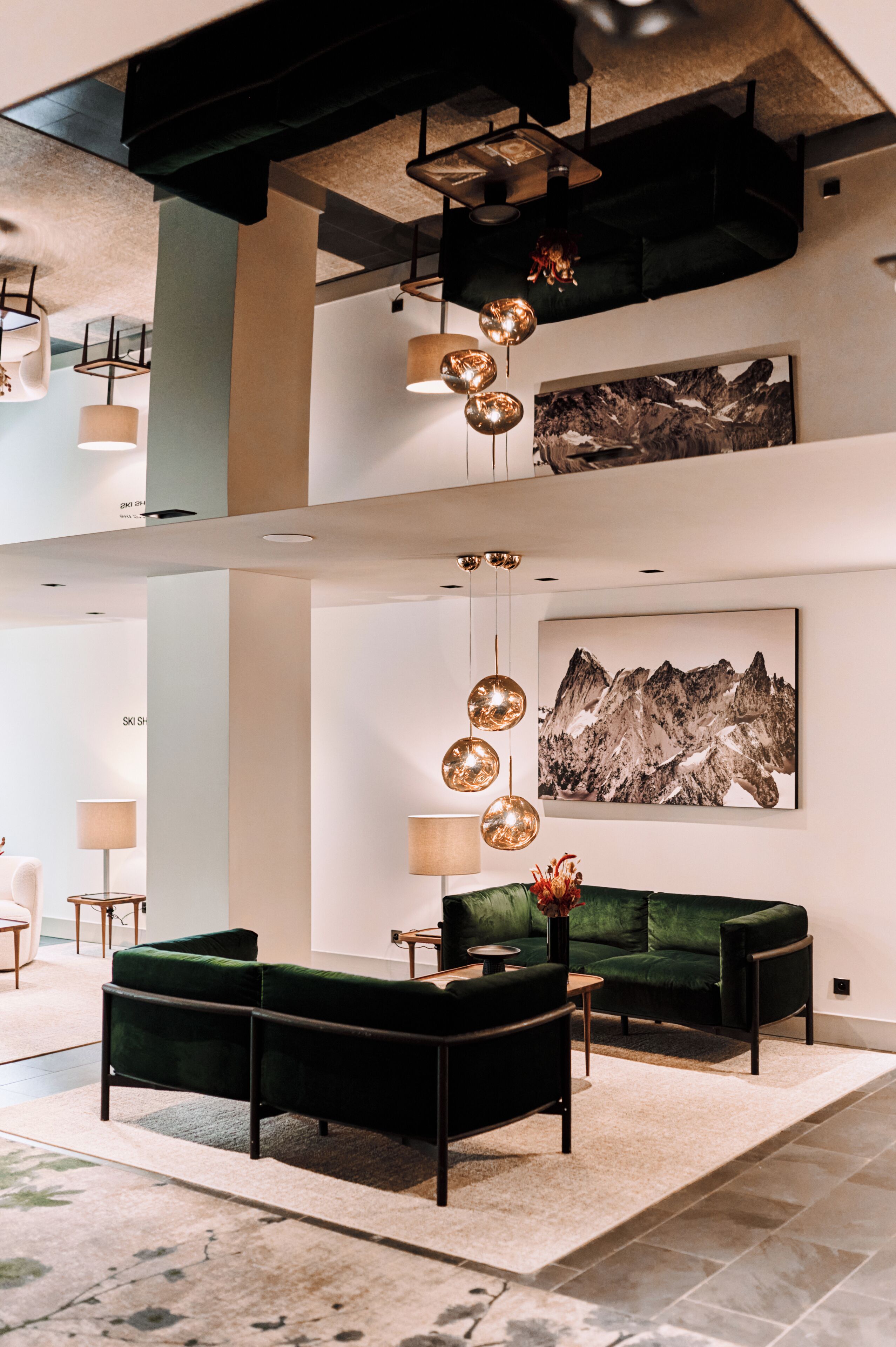 Eine moderne Lobby mit einem grünen Sofa, einem großen Berggemälde und einer ungewöhnlichen, kugelförmigen Leuchte.