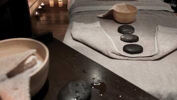 Une salle de spa équipée d’une table de massage, d’un bol en bois et de plusieurs pierres lisses disposées sur une surface humide.