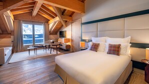 Une chambre d’hôtel avec un grand lit, un bureau et une chaise. Il y a une fenêtre donnant sur les montagnes.