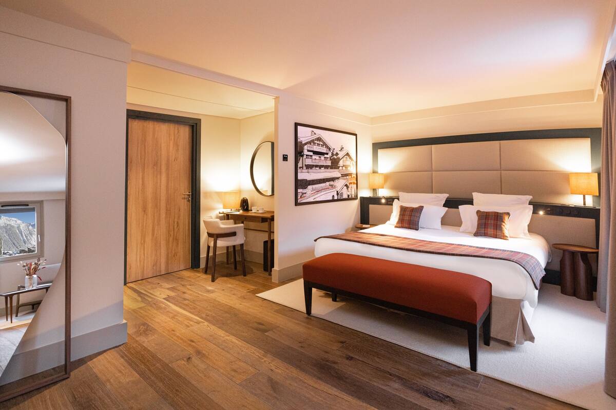 Hotelkamer met een groot bed, een bureau en een stoel. Er is een raam met uitzicht op bergen.