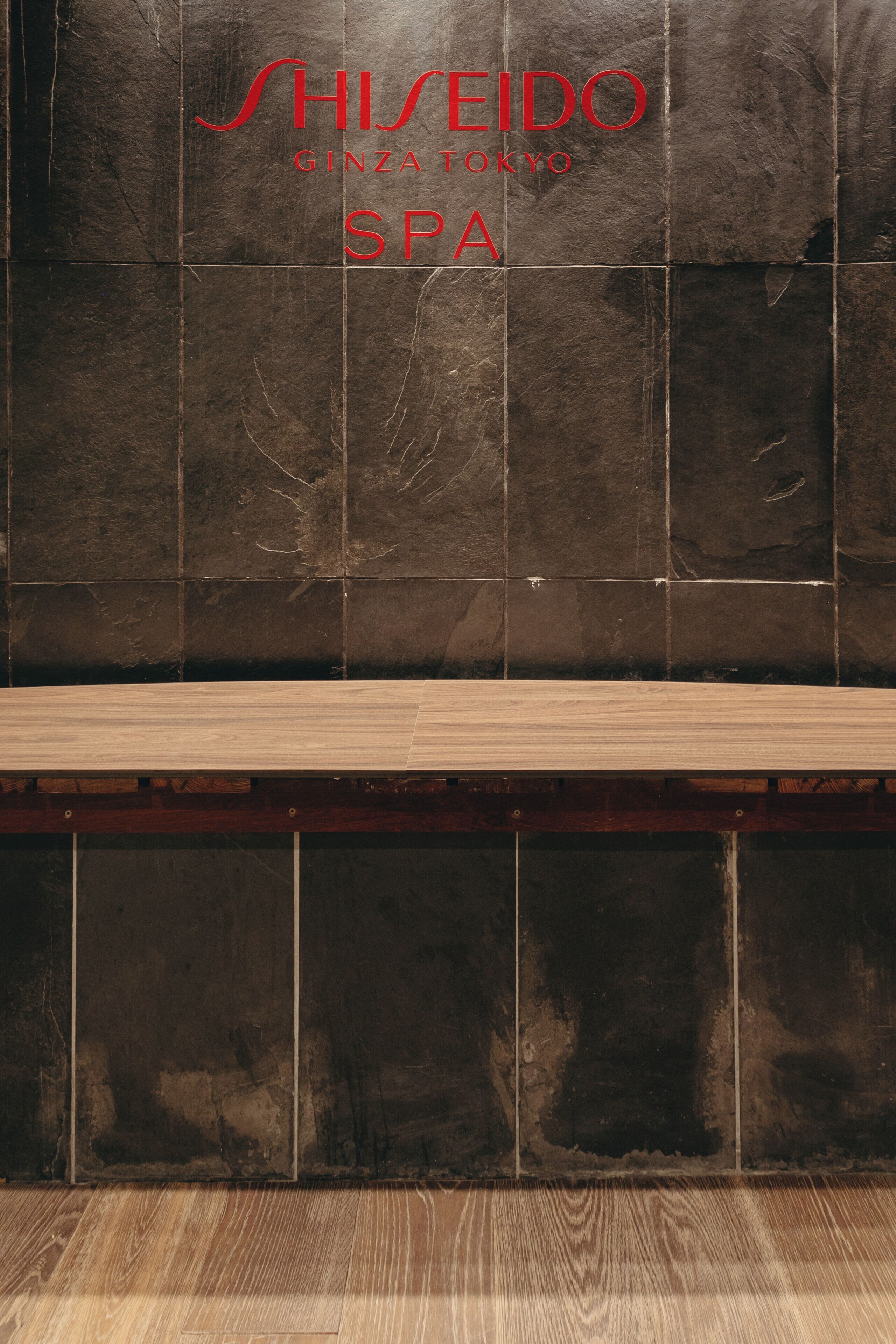 En flisevæg med teksten 'SHISEIDO GINZA TOKYO SPA' og en træbænk foran.