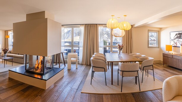 Un vaste salon doté d’une cheminée, un coin repas avec une grande table et des chaises, et une cuisine équipée d’un meuble en bois.