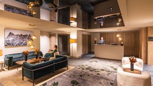 Un hall d’hôtel comprenant un comptoir d’accueil, un espace salon et un grand tableau représentant des montagnes.