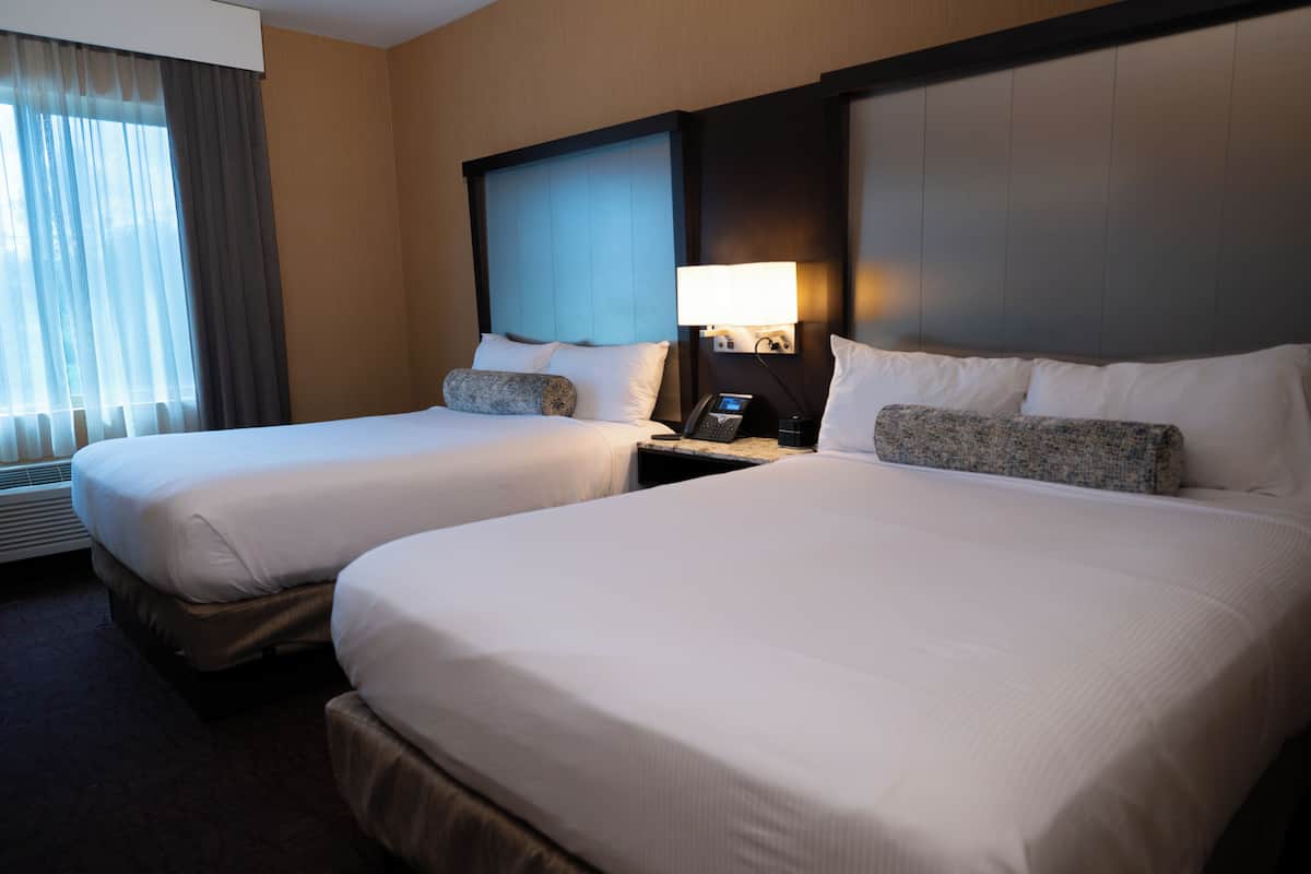 Una habitación de hotel con dos camas, una mesita de noche con lámpara y una ventana con cortinas.