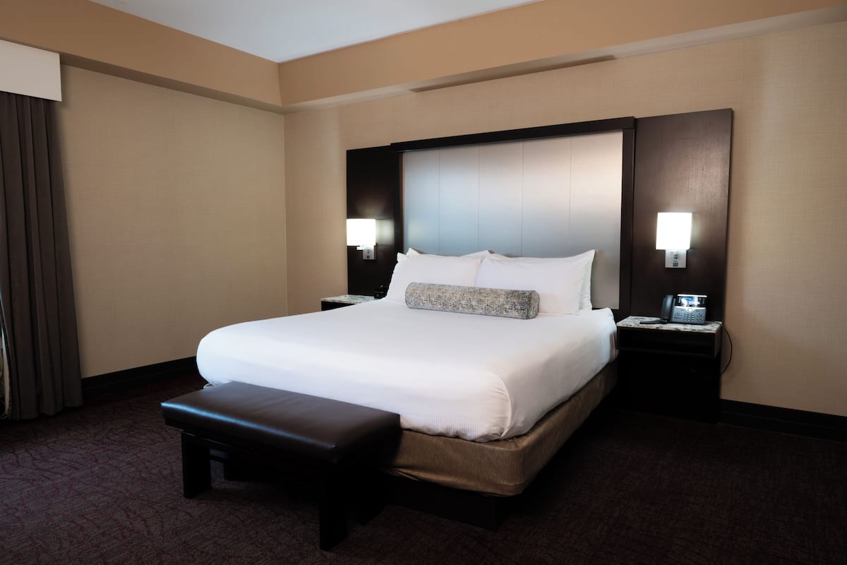 Habitación de hotel con una cama grande, una mesita de noche con lámpara, un banco y un teléfono instalado en la pared.
