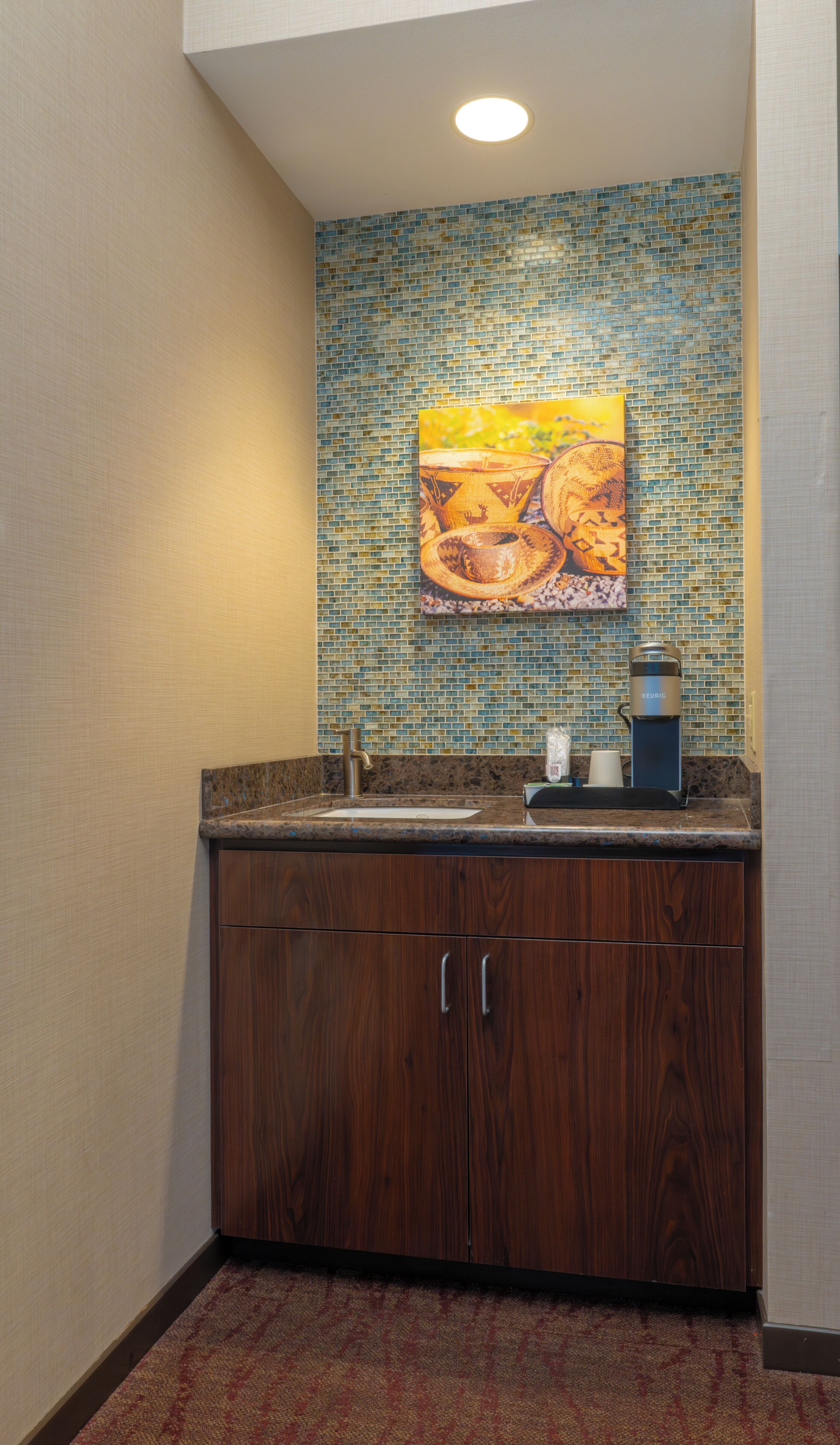A bathroom with a mosaic tile backsplash, a sink, a coffee maker, and wooden cabinets.