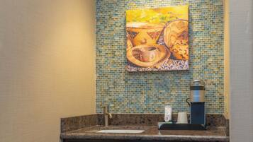 A bathroom with a mosaic tile backsplash, a sink, a coffee maker, and wooden cabinets.