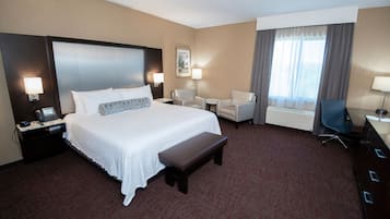 Habitación de hotel con una cama grande, mesitas de noche, un escritorio, una silla y una ventana con cortinas.