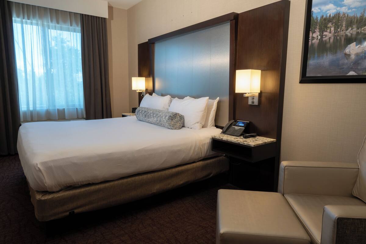 Habitación de hotel con una cama grande, dos lámparas de noche, un teléfono, una silla y un cuadro en la pared.