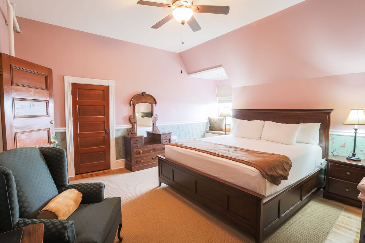Une chambre à coucher avec un grand lit, une commode, une chaise et un ventilateur de plafond.