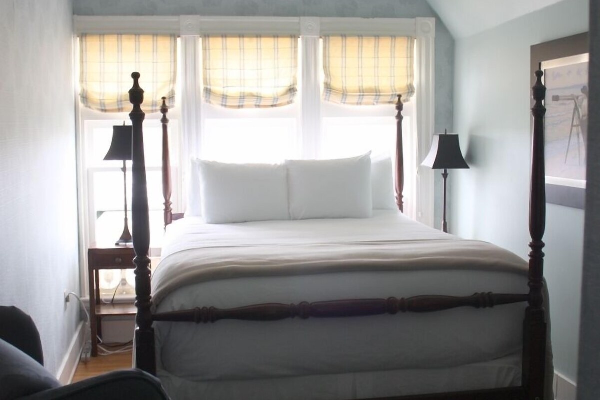 A bedroom with a large bed, a chair, a nightstand, and a window with curtains.