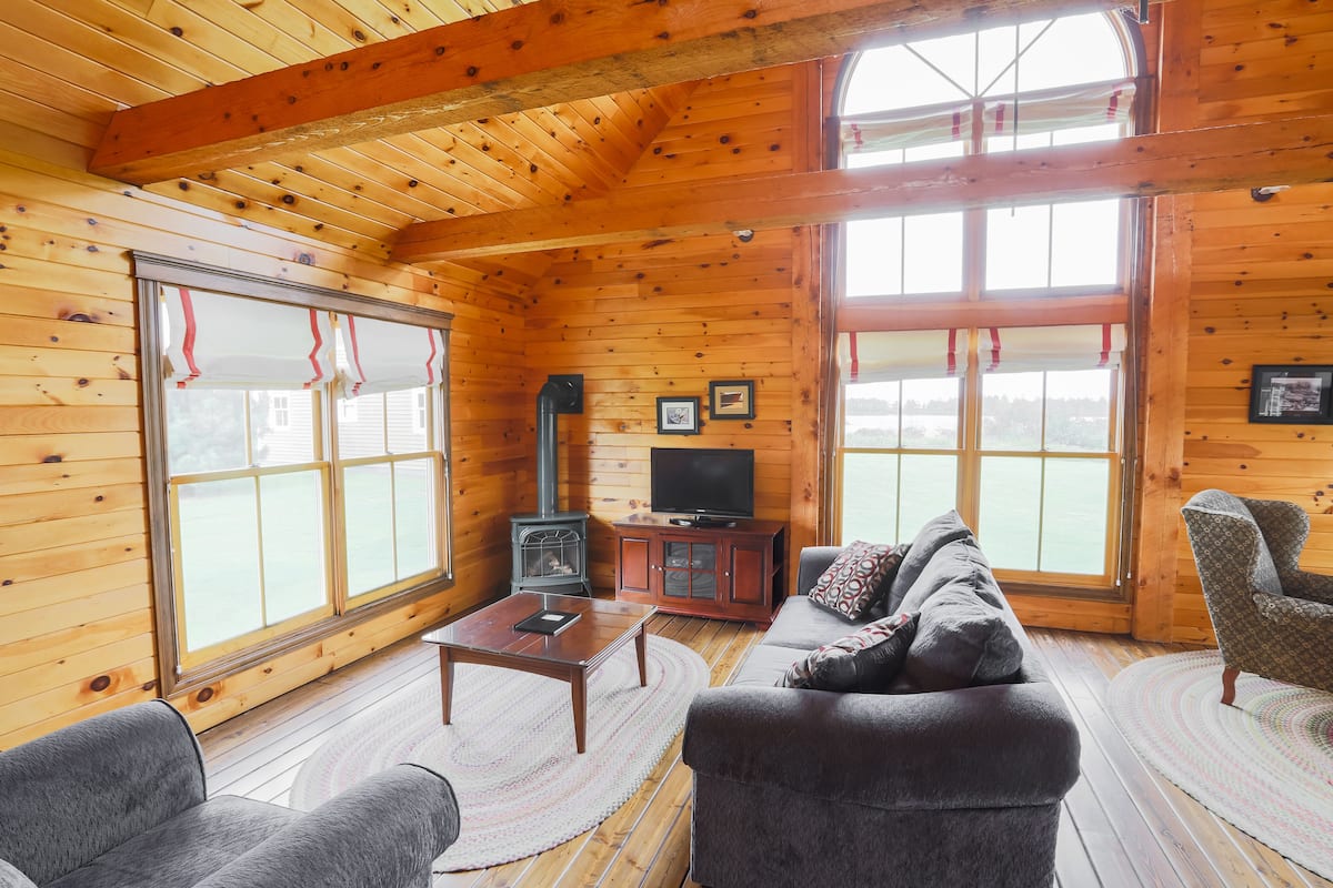 L’intérieur chaleureux d’un chalet, avec un revêtement mural en bois, un canapé, un fauteuil, un téléviseur et une cheminée.
