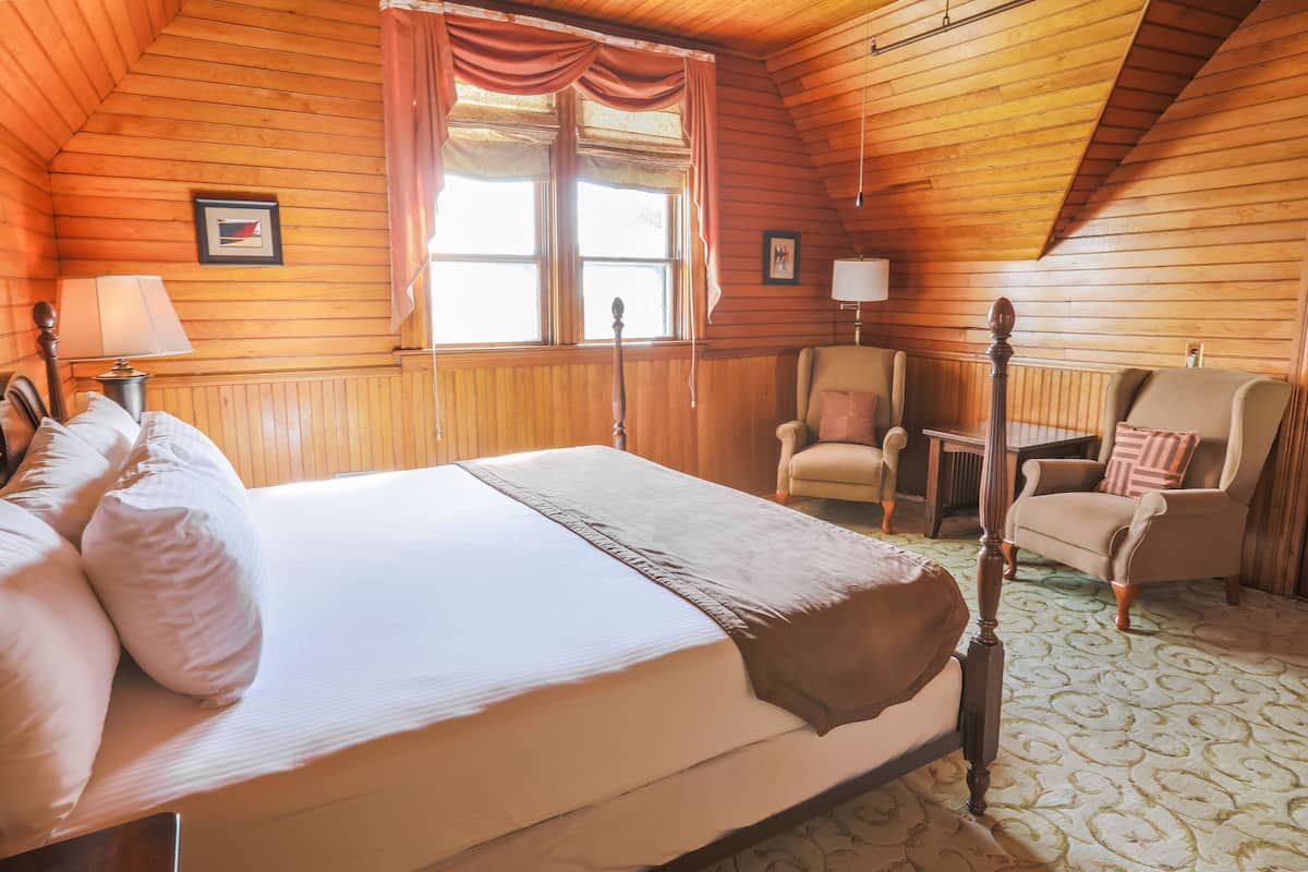Une pièce confortable avec un grand lit, une chaise, une table et une fenêtre avec des rideaux.
